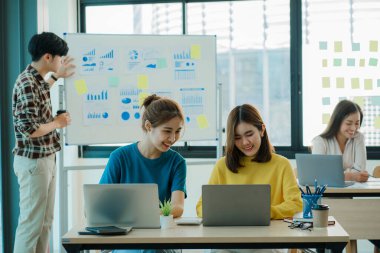 Bir grup Asyalı genç iş adamı yeni nesil yaratıcı genç dizüstü bilgisayarlara beyin fırtınası yapıyor. Toplantıda yeni başlatılan projeler için fikir alışverişinde bulunun ve tartışın.