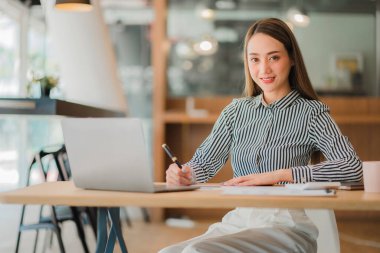 Asian businesswoman using her laptop calculator to make money on her desk math, tax, accounting, statistical reports, and analytical research ideas. Modern office real estate investment information