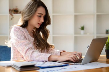 Asian businesswoman using her laptop calculator to make money on her desk math, tax, accounting, statistical reports, and analytical research ideas. Modern office real estate investment information