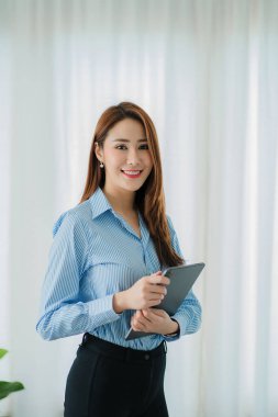 Dijital tablet kullanan neşeli, kendinden emin, profesyonel, güzel Asyalı genç bir iş kadını bir ofis binasında online bir iş fikrini temsil ediyor..