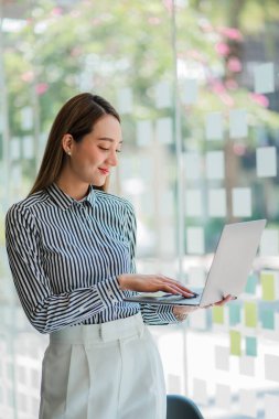 Portrait of smiling Asian businesswoman standing with laptop in her office work. Business concept. Financial accounting.