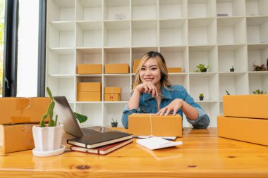 Starting a small business, SME entrepreneur or freelance, young Asian woman using a laptop computer with a box. successful women at work Shipping, Packaging, Online Marketing, SME Business Ideas