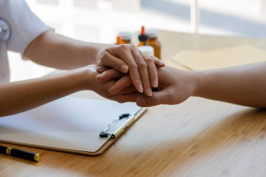 Asyalı kadın doktor masada el sıkışarak hastaları teşvik ediyor ve onlara danışıyor.