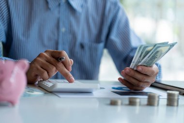 man holding a dollar bill use money calculator Keep a record of the amount of money he accumulates throughout the year with piles of coins and piggy banks for future business investments.