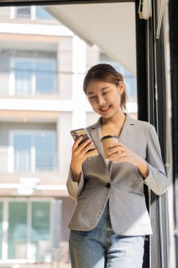 Başarılı genç Asyalı kadın işten çıkarken cep telefonuyla konuşuyor. Reklam metninizin ya da tanıtım materyalinizin kopyalama alanının yanında dururken