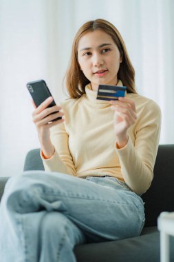 Güzel Asyalı kadın internet sitesinden alışveriş yapıyor ve kredi kartını ödeme için kullanıyor. İnternetten alışveriş yapmak, kanepede oturmak.