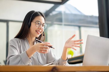 Asyalı üniversite öğrencisi kablosuz kulaklık takıyor ve internet üzerinden dil öğrenmek için dizüstü bilgisayara yazıyor. İzleyin ve hoparlörlerin laptop webinar, video çağrısı ve evde e-öğrenim konseptini dinleyin.