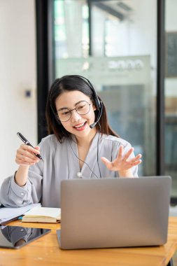 Asyalı üniversite öğrencisi kablosuz kulaklık takıyor ve internet üzerinden dil öğrenmek için dizüstü bilgisayara yazıyor. İzleyin ve hoparlörlerin laptop webinar, video çağrısı ve evde e-öğrenim konseptini dinleyin.