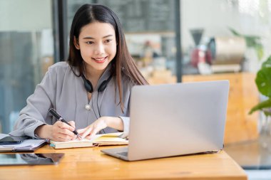 Asyalı öğrenciler internetten dil öğrenmek için boyunlarına kablosuz kulaklık takıp dizüstü bilgisayarlar yazıyorlar. İzle ve laptop webinarlarını dinle. Video çağrısı ve evde e-öğrenim fikirleri