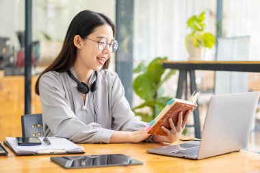 Asyalı öğrenciler internetten dil öğrenmek için boyunlarına kablosuz kulaklık takıp dizüstü bilgisayarlar yazıyorlar. İzle ve laptop webinarlarını dinle. Video çağrısı ve evde e-öğrenim fikirleri