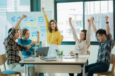 Genç Asyalı iş grupları mutlu ve başarılı hissediyorlar. İş hedeflerindeki başarıları kutlamak için gülen eller masadaki dizüstü bilgisayarla ve ofisteki finans grafiğiyle uğraşır.