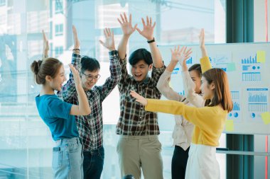 Genç Asyalı iş grupları mutlu ve başarılı hissediyorlar. İş hedeflerindeki başarıları kutlamak için gülen eller masadaki dizüstü bilgisayarla ve ofisteki finans grafiğiyle uğraşır.