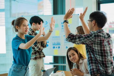 Genç Asyalı iş grupları mutlu ve başarılı hissediyorlar. İş hedeflerindeki başarıları kutlamak için gülen eller masadaki dizüstü bilgisayarla ve ofisteki finans grafiğiyle uğraşır.