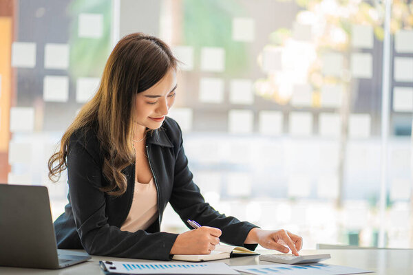 Портрет азиатской предпринимательницы, работающей на ноутбуке и финансовых графиках на рабочем месте. Азиатская работница независимого интернет-маркетинга Электронная коммерция Телемаркетинг Идеи Отчет