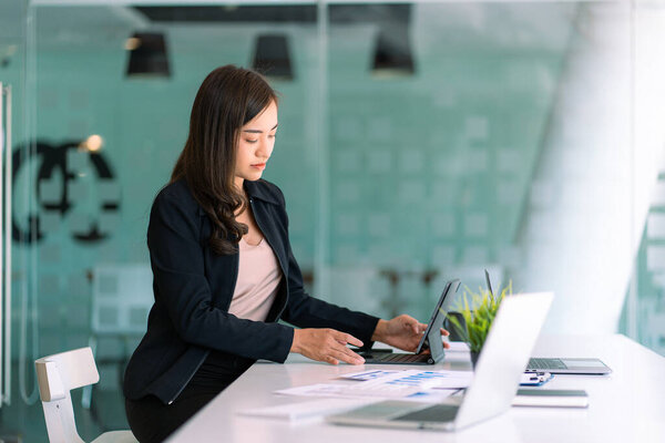 Portrait of Asian businesswoman working on her laptop computer and financial graphs in her workstation. Asian girl employee independent online marketing Ecommerce Telemarketing Ideas Report