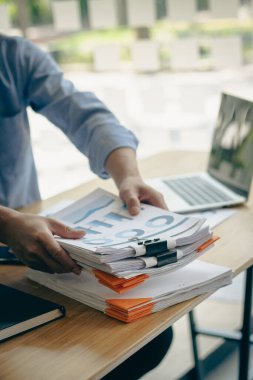 Genç işadamı kağıt yığınları içinde çalışıyor, bilgi, iş raporları ve modern ofisteki dizüstü bilgisayar masasında tamamlanmamış kağıt yığınları arıyor, portre fotoğrafı.