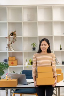 KOBİ Girişim Fikirleri, Genç Girişimciler, küçük işletme sahipleri evde dizüstü bilgisayar ve kutu paketleme ve teslimat durumuyla çalışıyorlar. Küçük işletme sahibi kadın malları kutulara koyuyor.