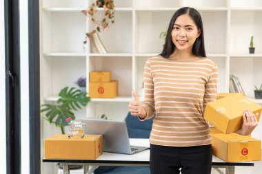 KOBİ Girişim Fikirleri, Genç Girişimciler, küçük işletme sahipleri evde dizüstü bilgisayar ve kutu paketleme ve teslimat durumuyla çalışıyorlar. Küçük işletme sahibi kadın malları kutulara koyuyor.