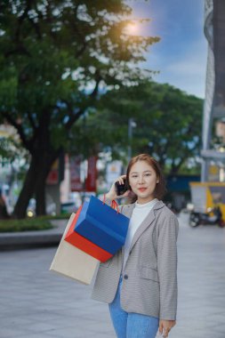 Alışveriş merkezinin önünde duran mutlu Asyalı kadın. - Evet. Alışveriş torbaları tutan Asyalı kadın, kadın konsept alışveriş standı ve dikey olarak elinde çok renkli kağıt torbalar..
