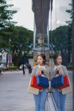 Alışveriş merkezinin önünde duran mutlu Asyalı kadın. - Evet. Alışveriş torbaları tutan Asyalı kadın, kadın konsept alışveriş standı ve dikey olarak elinde çok renkli kağıt torbalar..