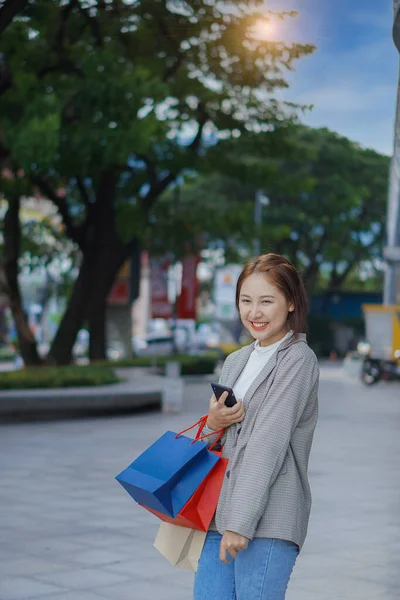 ショッピングセンターのショッピングモールの前に立つ幸せなアジアの女性 そうだ アジアの女性はショッピングバッグ 女性のコンセプトショッピングスタンドを保持し 垂直多色の紙袋を保持 — ストック写真
