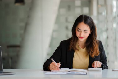 Sırıtkan Asyalı güzel iş kadını dizüstü bilgisayarı ve evrak işleriyle uğraşıyor. Hesap analizi, emlak yatırımları, finansal ve vergi sistemi kavramları hakkında rapor hazırlıyor.
