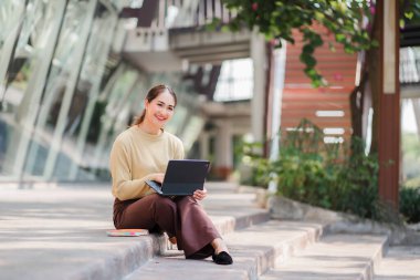 Tablet oynayan Asyalı kız üniversite öğrencisi yanında bir çantayla internette online öğrenme fikirleri arıyor..