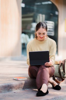 Tablet oynayan Asyalı kız üniversite öğrencisi yanında bir çantayla internette online öğrenme fikirleri arıyor..