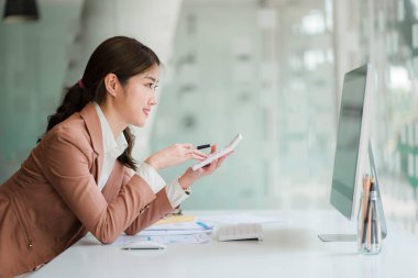 Ofiste bilgisayar başında oturan Asyalı çekici iş kadını Milli Gelir İdaresi belgelerindeki miktarın hesaplanması hakkında bir rapor hazırla.