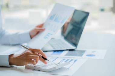 Muhasebe masasında bir muhasebeci, aylık mali raporlar veya şirket kârları oluşturmak için yatırım grafiklerini analiz etmesi için hesap makinesine baskı yapar..