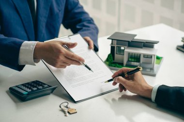Bir emlakçı ya da satış müdürü satış sunar ve ev satın alma sözleşmesi ve ücretsiz sigorta şartlarını açıklar. İpotek konsepti ve emlak satış sonrası servisi