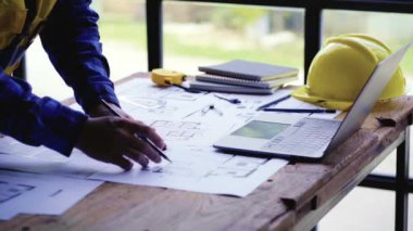 Cetvel, kalem, mezura, mezura, mimar şapkası ve diğer masa aksesuarlarıyla bina veya mimari çizimler yapan genç bir mühendis..