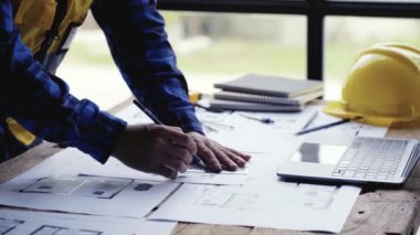 Cetvel, kalem, mezura, mezura, mimar şapkası ve diğer masa aksesuarlarıyla bina veya mimari çizimler yapan genç bir mühendis..