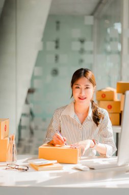 Asyalı kız KME küçük işletme girişimcileri Online satış konsepti, Mutlu Asyalı iş sahibi evde bilgisayar ve kutular üzerinde çalışıyor, KME paket kutularını dikey müşterilere teslim ediyor.