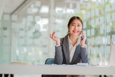 Akıllı telefon tutan Asyalı iş kadını, elinde kalem, dizüstü bilgisayar ve hesap makinesiyle grafiği gösteren bir raporu analiz ediyor. İş istasyonunda, muhasebede, çevrimiçi pazarlama konseptinde, e-ticarette, manzara resminde.