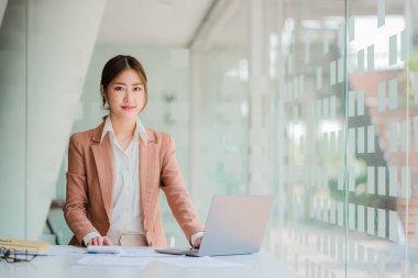 Asyalı iş kadını, grafiği gösteren bir raporu kalem, dizüstü bilgisayar ve hesap makinesiyle analiz ediyor. İş istasyonu muhasebecisinde çevrimiçi pazarlama konsepti eTicari manzara