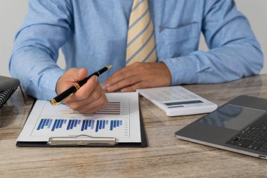 Yakın plan fotoğraf. Elinde kalem tutan ve finansal belgelere finansal pazarlama ağı şeması olan ve dizüstü bilgisayar üzerinde çalışan bir iş adamı. çevrimiçi muhasebe kavramı