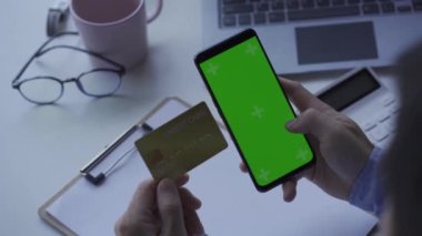 Yeşil ekran ve kredi kartıyla akıllı telefonu tutan bir adamın yakın çekimi. Ev bankacılığı konseptinde online alışveriş ve evde yaşam tarzı.
