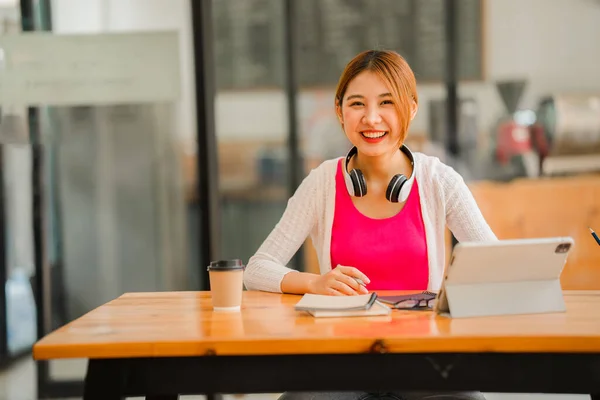 Asian female student studying online, e-learning with tablet sitting at desk and holding pen, happy Asian elementary school girl smiling at camera, thinking about distance learning.