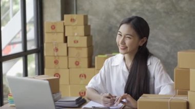 İş kadını müşteriye sevkiyat için adres yazıyor ve ev sahibi küçük işletme sahibi sme parsel dağıtım girişimcisi 4k video başlatarak dizüstü bilgisayardaki çevrimiçi iş işleri notlarını kontrol ediyor