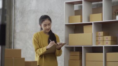İş kadını müşteriye sevkiyat için adres yazıyor ve ev sahibi küçük işletme sahibi sme parsel dağıtım girişimcisi 4k video başlatarak dizüstü bilgisayardaki çevrimiçi iş işleri notlarını kontrol ediyor