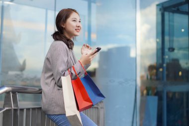 Alışveriş merkezinin zemininde alışveriş torbaları taşıyan gülümseyen Asyalı kadın. Kadın modası, alışveriş, yaşam tarzı, mutluluk, tüketim, satış ve insan kavramı.