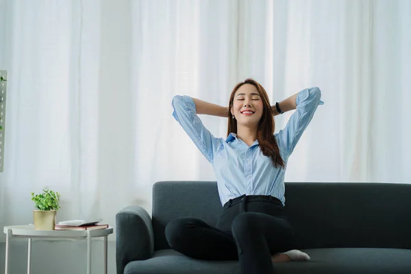 smiling asian woman relaxing sitting on sofa at home Relaxed lifestyle woman enjoying luxury sofa on living room.