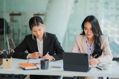 İki Asyalı iş kadını dijital tablet kullanarak yeni başlangıç projesi fikirlerini tartışıyor. Ofisteki finans ve yatırım piyasalarının planlama ve istatistiklerini analiz et.
