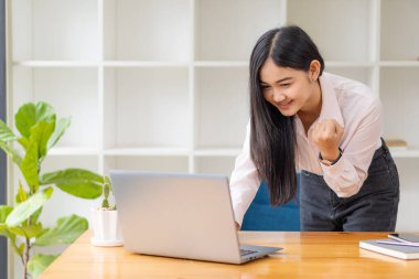 Güzel bir Asyalı kadın ofiste dizüstü bilgisayar kullanırken kutlama yapar ve iş başarısı için onu tebrik eder..