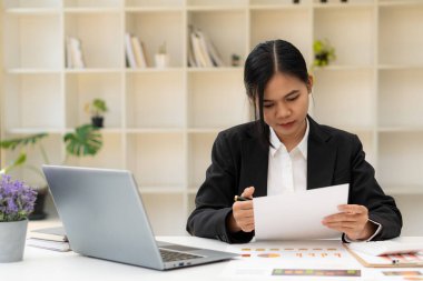 Modern masada çalışan Asyalı bir iş kadınının portresi bilgisayar kontrolü şirketinin mali belgelerini kullanıyor. Çevrimiçi pazarlama kavramı.