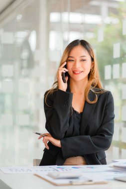 İş yerinde bilgisayar kullanan Asyalı iş kadınları iş planı raporlarını ofiste hazırlamaya başlarlar. Genç girişimci akıllı telefondan konuşuyor. Resmi danışman dikey resim