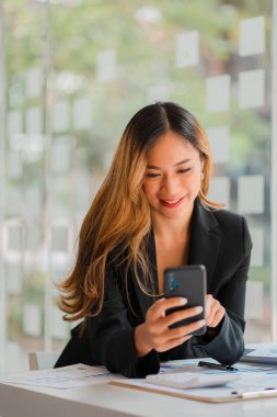 İş yerinde bilgisayar kullanan Asyalı iş kadınları iş planı raporlarını ofiste hazırlamaya başlarlar. Genç girişimci akıllı telefondan konuşuyor. Resmi danışman dikey resim