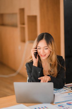 İş yerinde bilgisayar kullanan Asyalı iş kadınları iş planı raporlarını ofiste hazırlamaya başlarlar. Genç girişimci akıllı telefondan konuşuyor. Resmi danışman dikey resim