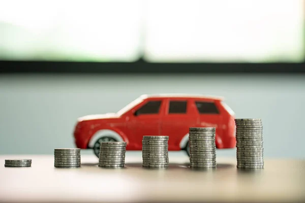 The red car is behind the pile of coins. all on the wooden table money saving ideas close-up images Save money for new car purchases, savings and car loans.